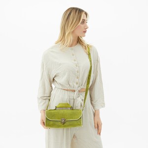 The green leather bag is worn crossbody by the woman.