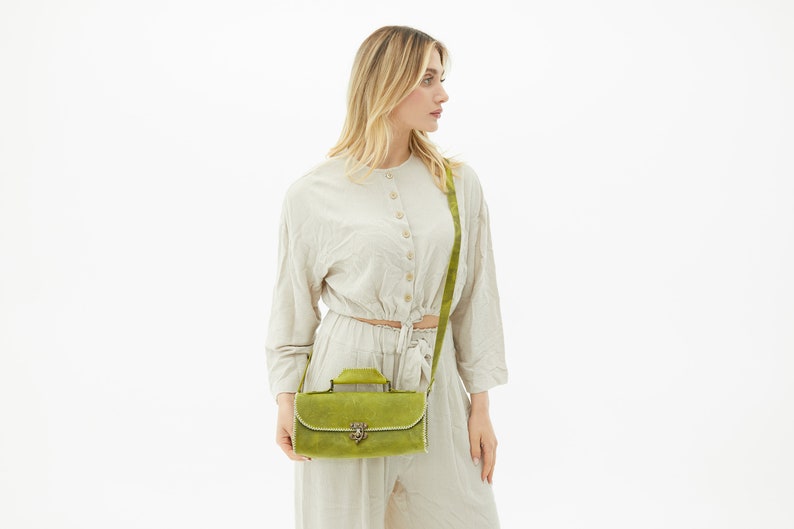 The green leather bag is worn crossbody by the woman.