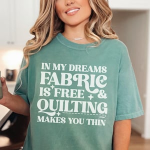 Op de afbeelding: Lichtgroen T-shirt met de witte tekst "IN MY DREAMS FABRIC IS FREE & QUILTING MAKES YOU THIN". Het shirt is effen van kleur en heeft korte mouwen. De woorden "Light Green" staan linksonder in de afbeelding.