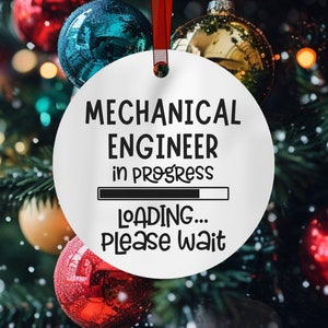 May include: White round Christmas ornament with black text that reads "Mechanical Engineer in progress" with a progress bar and "Loading... Please wait". The ornament is hanging on a Christmas tree with red and gold ornaments.