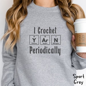 This Funny Crocheting Sweatshirt is a Gildan 18000 crewneck sweatshirt in the color Sport Grey. The text on front says I Crochet Yarn Periodically with the word Yarn spelled out in the periodic table.