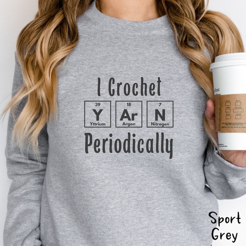 This Funny Crocheting Sweatshirt is a Gildan 18000 crewneck sweatshirt in the color Sport Grey. The text on front says I Crochet Yarn Periodically with the word Yarn spelled out in the periodic table.