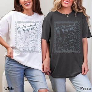 以下が含まれることがあります： 白とペッパー色の2枚のTシャツ。それぞれに、水色の切手のようなデザインが施されています。デザインには、「professional yapper」と「speech language pathologist Mrs. Smith」の文字と、さまざまなスピーチ関連のイラストが含まれています。
