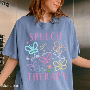 Puede incluir: Camiseta azul vaquero con las palabras "SPEECH THERAPY" en rosa. La camiseta presenta gr&aacute;ficos de mariposas en varios colores y la frase "helps little voices take flight".