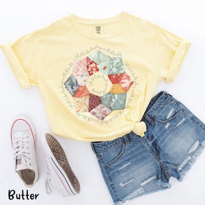 May include: A yellow t-shirt with a floral print and the text "I still like to play with blocks" repeated around the print.