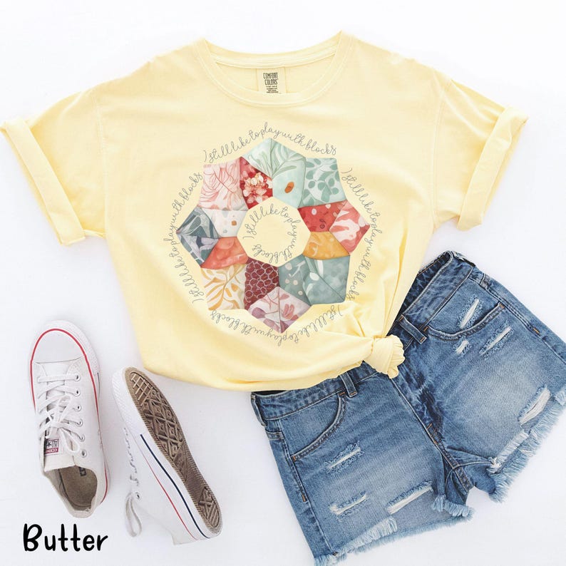 May include: A yellow t-shirt with a floral print and the text "I still like to play with blocks" repeated around the print.