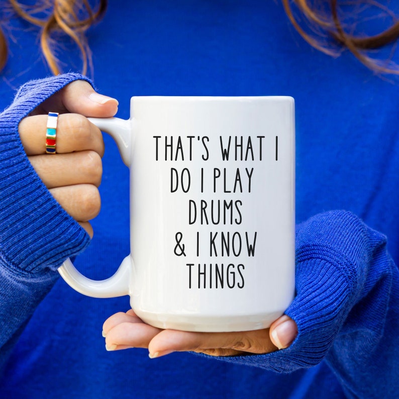 May include: White ceramic coffee mug with black text that reads "That's what I do I play drums & I know things".