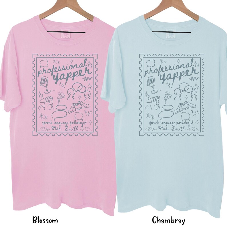 以下が含まれることがあります： 木製のハンガーに、半袖Tシャツが2枚、ブロッサムピンクとシャンブレーブルーで吊るされています。各シャツには、切手の枠の中に灰色のグラフィックがあります。グラフィックには、マイク、吹き出し、テキスト「professional yapper」が含まれています。