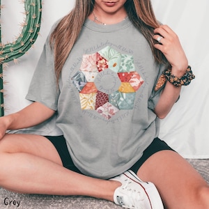 May include: A grey t-shirt with a floral design and the text "Little bits of joy with little bits of love" around the design.