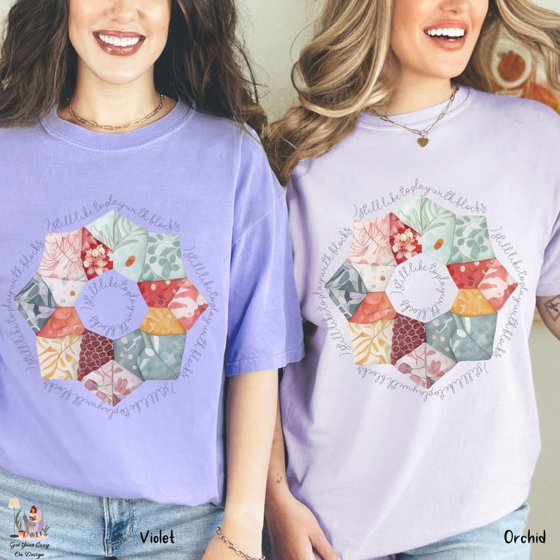 May include: Two women wearing purple t-shirts with a floral design and the text "I still like to play with blocks". The shirts are available in two colors: violet and orchid.