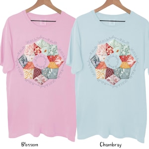 May include: Two t-shirts with a colorful patchwork design in the center. The design is a circle with the text "I still like to play with blocks" written around the outside. The t-shirt on the left is pink and the t-shirt on the right is light blue.