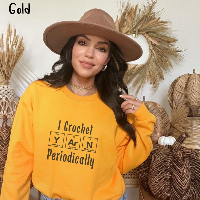This Funny Crocheting Sweatshirt is a Gildan 18000 crewneck sweatshirt in the color Gold. The text on front says I Crochet Yarn Periodically with the word Yarn spelled out in the periodic table.