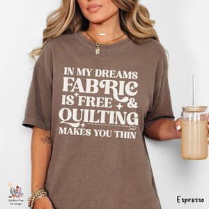 Op de afbeelding: Een bruin t-shirt met de tekst "IN MY DREAMS FABRIC IS FREE & QUILTING MAKES YOU THIN" in het wit. Het shirt is effen van kleur en heeft korte mouwen. Het woord "Espresso" staat rechtsonder afgedrukt.