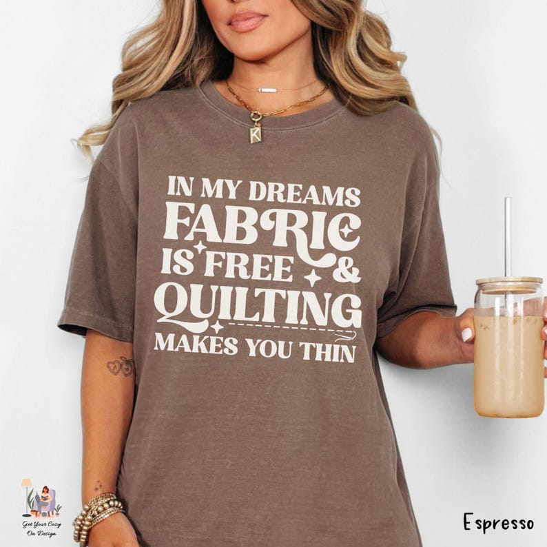 Op de afbeelding: Een bruin t-shirt met de tekst "IN MY DREAMS FABRIC IS FREE & QUILTING MAKES YOU THIN" in het wit. Het shirt is effen van kleur en heeft korte mouwen. Het woord "Espresso" staat rechtsonder afgedrukt.