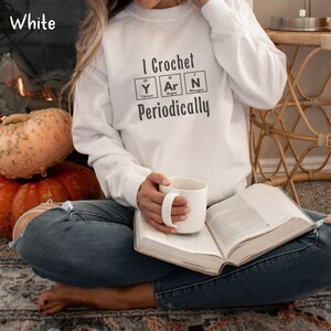 This Funny Crocheting Sweatshirt is a Gildan 18000 crewneck sweatshirt in the color White. The text on front says I Crochet Yarn Periodically with the word Yarn spelled out in the periodic table.