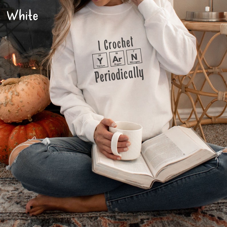 This Funny Crocheting Sweatshirt is a Gildan 18000 crewneck sweatshirt in the color White. The text on front says I Crochet Yarn Periodically with the word Yarn spelled out in the periodic table.