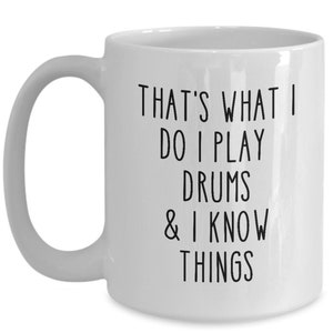 May include: White ceramic coffee mug with black text that reads "That's what I do I play drums & I know things".