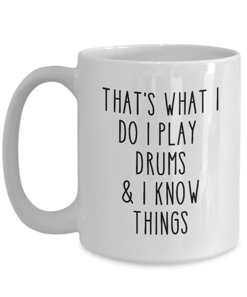 May include: White ceramic coffee mug with black text that reads "That's what I do I play drums & I know things".