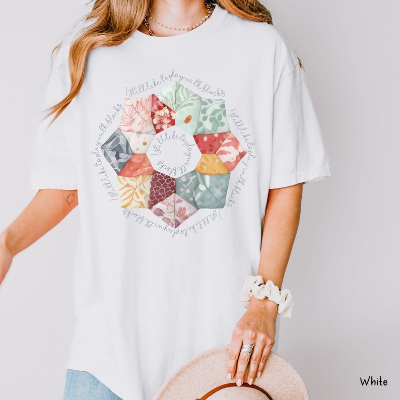 May include: White t-shirt with a colorful patchwork design and the text "I still like to play with blocks" repeated around the design.
