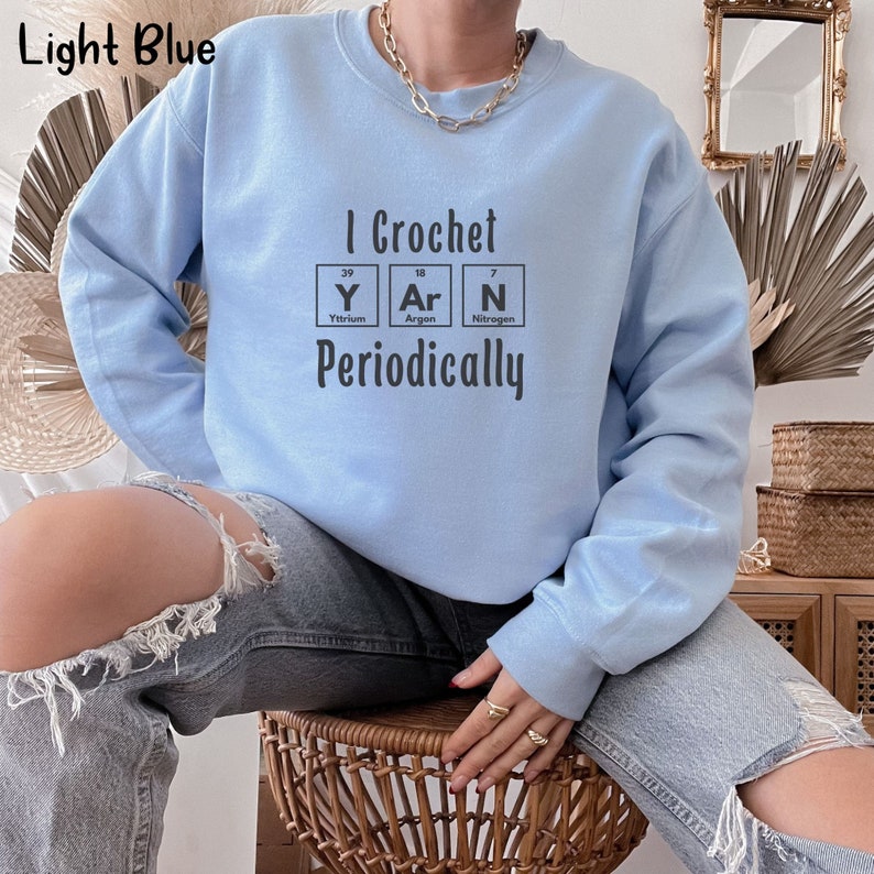 This Funny Crocheting Sweatshirt is a Gildan 18000 crewneck sweatshirt in the color Light Blue. The text on front says I Crochet Yarn Periodically with the word Yarn spelled out in the periodic table.