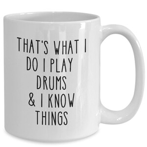 May include: White ceramic coffee mug with black text that reads "That's what I do I play drums & I know things"