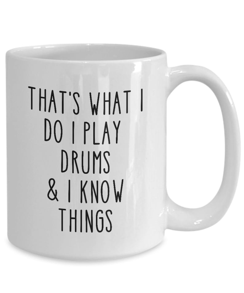 May include: White ceramic coffee mug with black text that reads "That's what I do I play drums & I know things"