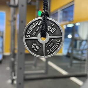 May include: A silver weight plate with the text "STANDARD ATHL. DEPT. 45 LB. 20.4 KG. MADE IN THE USA BARBELL" on it.