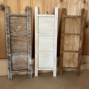 May include: Three wooden tiered shelves with a distressed whitewash finish, a natural wood finish, and a dark brown stain finish. Each shelf has three tiers and is freestanding.