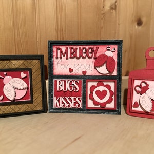May include: Three wooden signs with a ladybug theme. The signs are decorated with red and pink ladybugs, hearts, and the text "I'm buggy for you!" and "Bugs and Kisses".