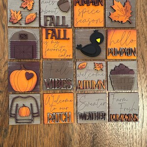 May include: A set of 12 wooden signs with fall-themed designs and sayings. The signs feature pumpkins, leaves, a bird, a barn, and text such as "nuts about fall", "pumpkin spice season", "fall vibes", and "welcome to our patch".