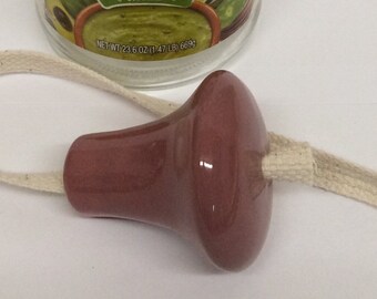 May include: A mauve ceramic bottle stopper with a white cotton wick attached. The stopper is shaped like a mushroom.