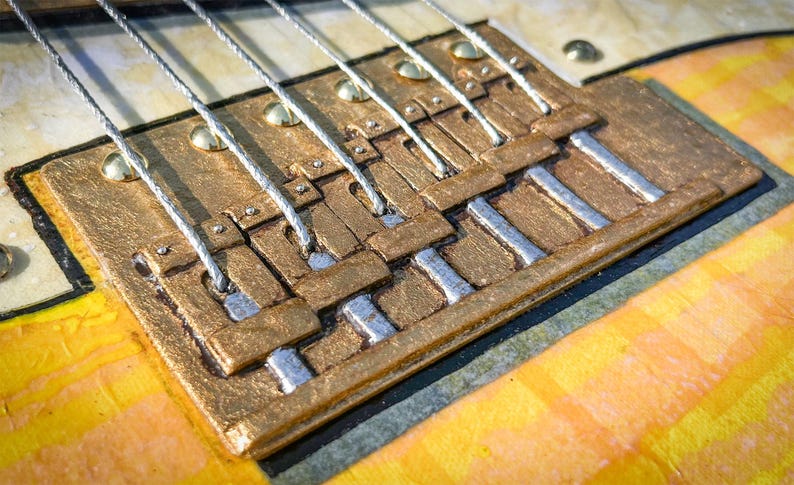Puede incluir: Un puente de guitarra con una base de metal texturizado de color dorado y seis selletas plateadas individuales. El puente est&aacute; montado sobre un cuerpo de guitarra a rayas amarillas claras y naranjas, con seis cuerdas plateadas sobre las selletas.