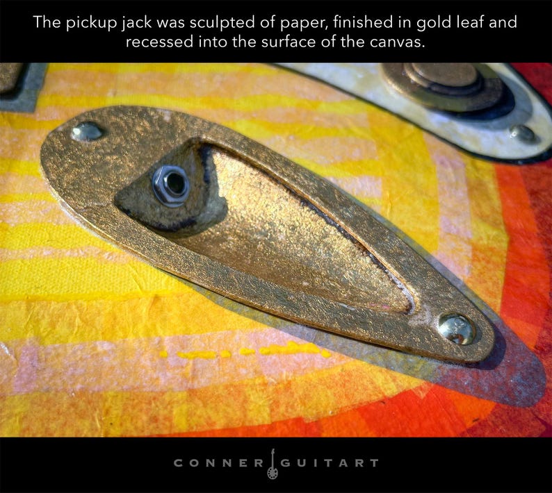 Puede incluir: Un jack de entrada esculpido en papel con acabado de pan de oro, empotrado en una superficie de lienzo con patrones amarillos y naranjas. El texto dice: The pickup jack was sculpted of paper, finished in gold leaf and recessed into the surface of the canvas.