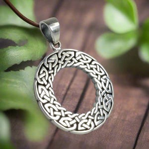 May include: A silver Celtic knot pendant with a circular design. The pendant is on a brown leather cord.