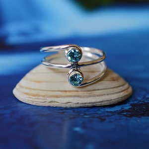 May include: A silver ring with two light blue gemstones. The ring is sitting on a white seashell.