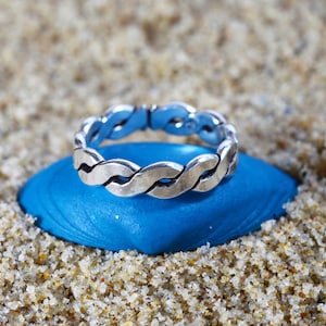 Pode incluir: Um anel de prata trançado sobre um fundo azul. O anel é feito de uma banda de metal trançada.