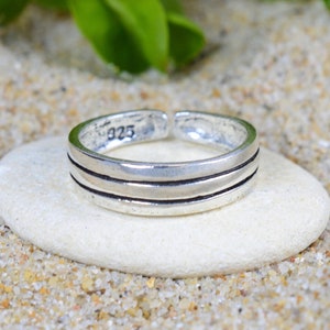 May include: A silver toe ring with three horizontal bands. The ring is marked with "925" on the inside.