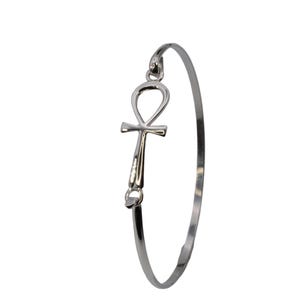 May include: A silver-colored bangle bracelet featuring an Ankh symbol. The Ankh, a symbol of life, is attached to the bracelet's band. The bracelet is a simple, elegant design, suitable for everyday wear.