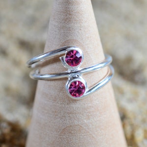 Puede incluir: Un anillo de plata con dos piedras de cristal rosa. El anillo está diseñado con dos bandas que se cruzan y se retuercen.