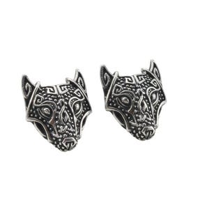 May include: Two silver-colored, detailed wolf head-shaped earrings. Each earring features an intricate design with geometric patterns and a textured finish. The earrings are displayed against a white background.