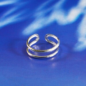 May include: A silver double-band toe ring. The ring is made of two thin bands of metal that are joined together at the top and bottom.