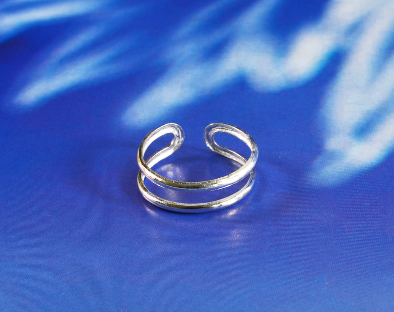 May include: A silver double-band toe ring. The ring is made of two thin bands of metal that are joined together at the top and bottom.