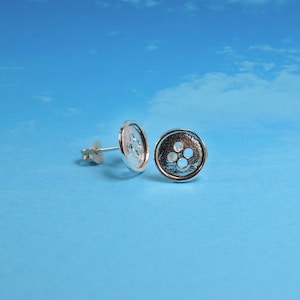 Puede incluir: Un par de pendientes de botón de plata con cuatro agujeros en cada botón.