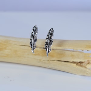 Op de afbeelding: Een paar zilveren veren oorbellen. De oorbellen zijn klein en delicaat, en ze hebben een eenvoudig ontwerp.