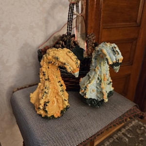 May include: Two decorative gourd-shaped ornaments with textured, warty surfaces. One is primarily yellow with green accents, and the other is light blue with yellow and green highlights. Both feature a curved, neck-like top section.
