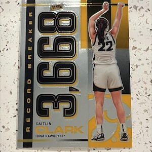 May include: A silver and gold basketball card featuring Caitlin Clark, a basketball player for the Iowa Hawkeyes. The card has a large number "388" printed on it and the text "Record Breaker".
