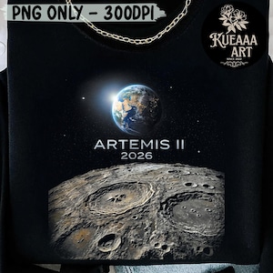 Puede incluir: Sudadera negra con un gráfico de la Tierra y la superficie lunar, con el texto "ARTEMIS II 2026". El diseño incluye un detalle de cadena dorada en el cuello y el logotipo de KUEAAA ART.