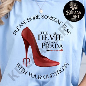 May include: Light blue t-shirt with the text "PLEASE BORE SOMEONE ELSE WITH YOUR QUESTIONS." The graphic features a red high heel shoe with a trident heel, the words "THE DEVIL WEARS PRADA," and a lipstick. A black circle with white flowers and text is in the upper right.