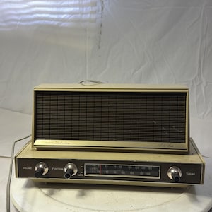 Puede incluir: Radio vintage Sears Silvertone con carcasa color crema y rejilla de altavoz marrón oscuro. La radio tiene un dial de sintonización, perillas de volumen y función, y las palabras "Solid State". Un dispositivo electrónico retro.