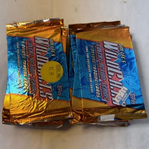 May include: Several unopened packs of "WildC.A.T.S. Covert Action Teams" trading cards. Each pack is gold and blue with text that reads "8 Deluxe Trading Cards" and "Look for Exclusive Prism Cards". The packs are from Topps.